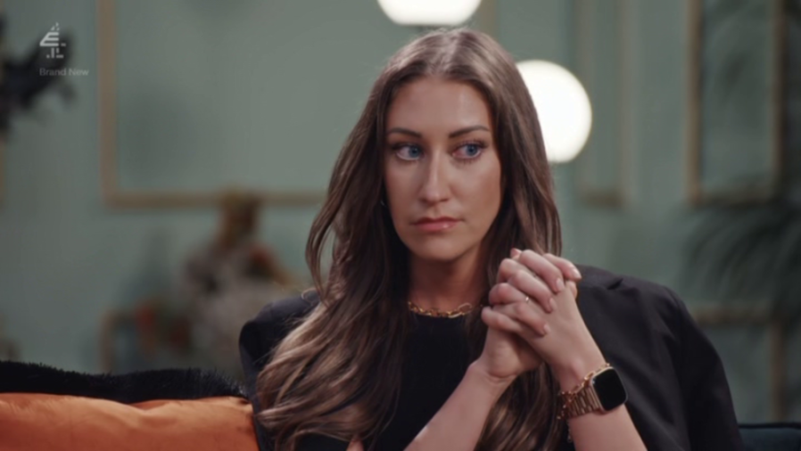 Hannah looking intently to the side, wearing a black top and a gold watch, with her hands clasped.