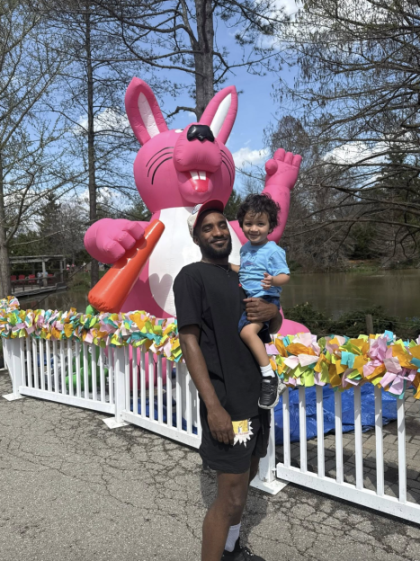 A man holding a child in front of a giant inflatable pink rabbit holding an orange carrot.