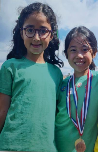 Nuria Sajjad and Selena Lau, two young school friends, smiling in their school sports day attire.