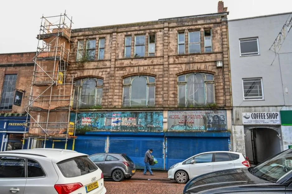 A dilapidated stone building in Dudley with boarded-up storefronts and scaffolding on the left.