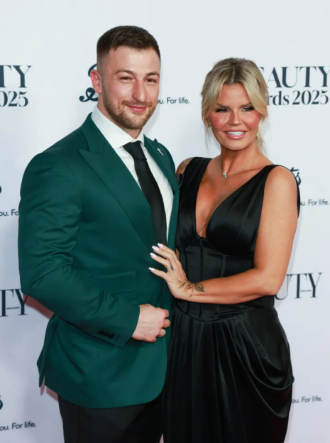 A man in a green suit and a woman in a black dress pose on a red carpet.