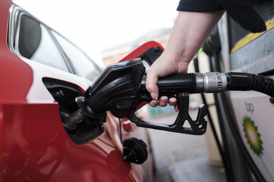 A woman's hand holding a fuel pump nozzle in a car's fuel tank, with a BP sign in the background.