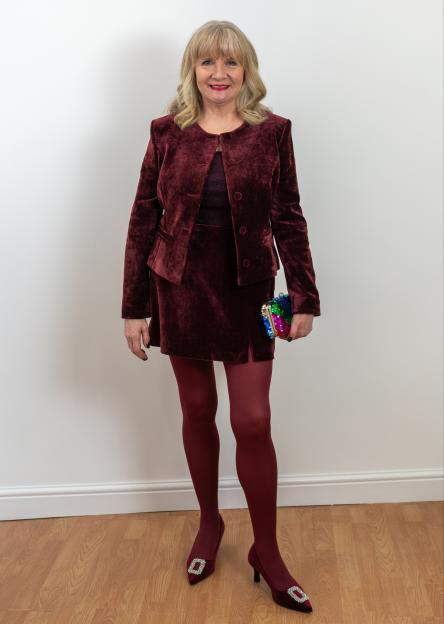 Julie Player in a maroon velvet suit, tights, and heels with a sequined clutch.