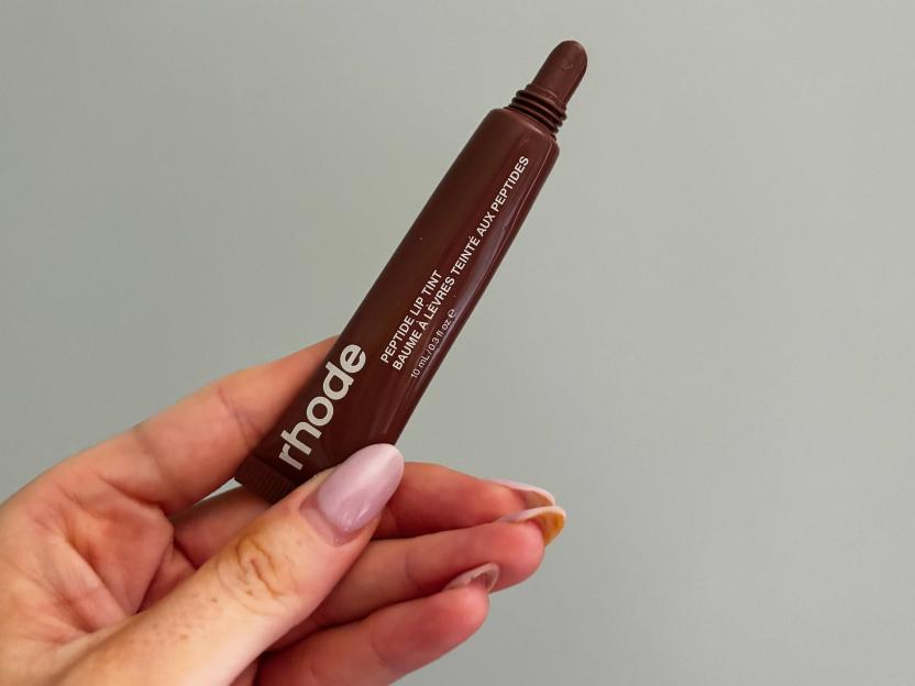 A hand holding a rhode Peptide Lip Tint in a brown tube.