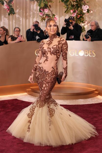 Jennifer Lopez on the red carpet in a long-sleeved, sheer brown dress with brown patterns and a cream-colored tulle mermaid skirt.