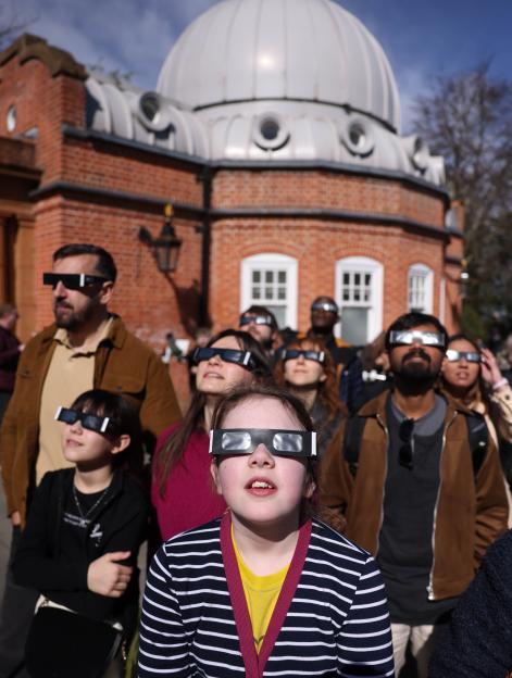People wearing protective glasses watch a partial solar eclipse at Greenwich Observatory in London.