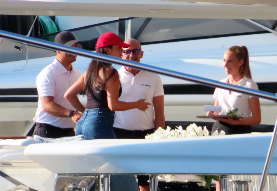 Georgina Rodriguez in a red baseball cap and blue jeans talking on a yacht with three other people.