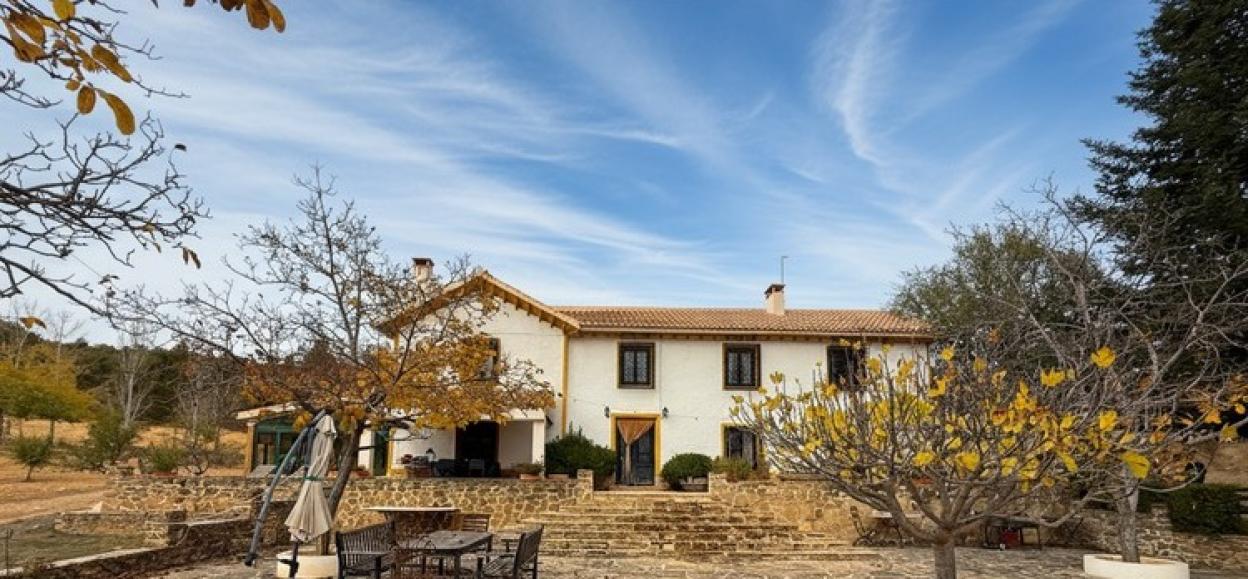 A white villa with a terracotta roof, surrounded by autumn trees and a stone patio.