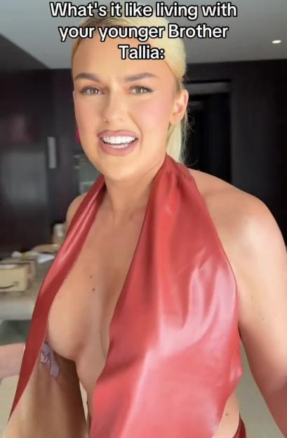 Tallia Storm in a red revealing dress, laughing as text above her reads "What's it like living with your younger Brother Tallia:"