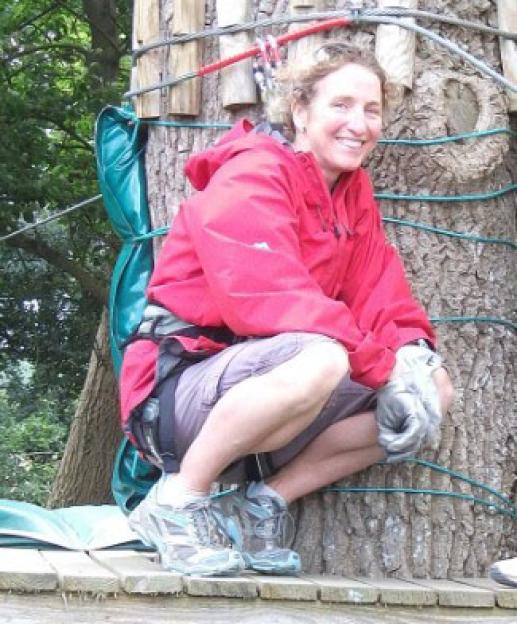 Liz Dobson in climbing gear, crouching by a tree.