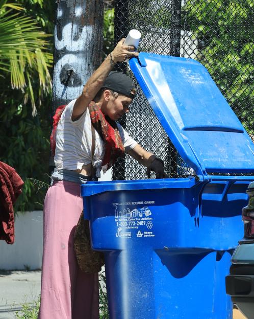 Loni Willison rummaging through a blue recycling bin in Los Angeles.
