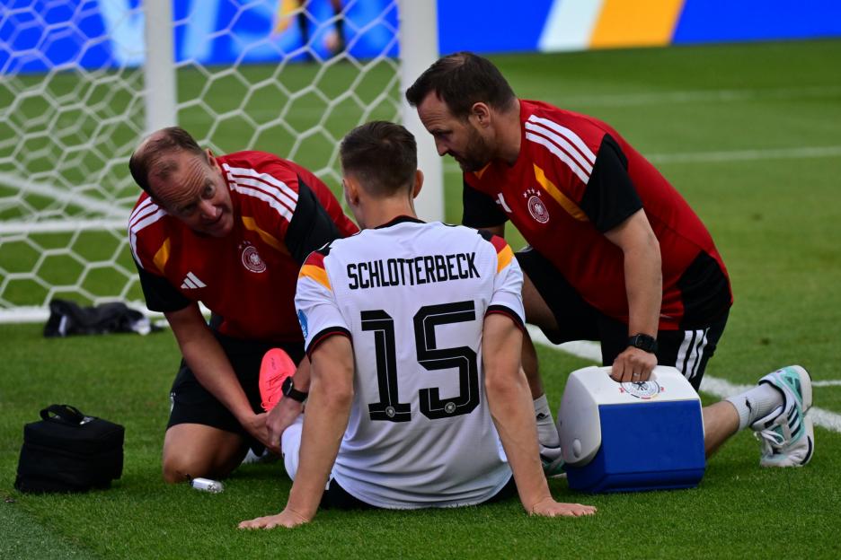 German soccer player Schlotterbeck sitting on the field receiving medical attention from two staff members.