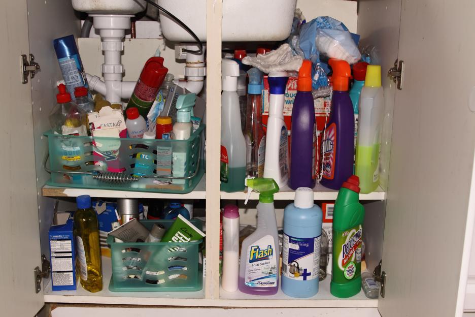 A kitchen cupboard beneath a sink, filled with cleaning supplies.
