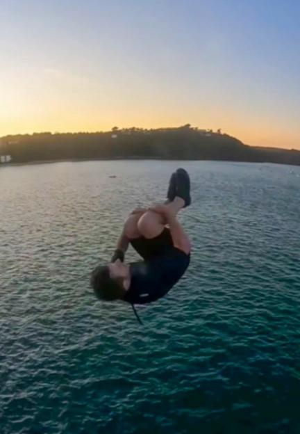 A man in a wetsuit performing a tuck dive over a body of water at sunset.