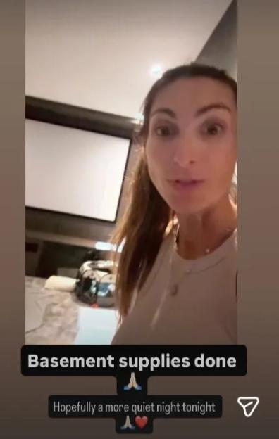 A person talking in what appears to be a basement, with a large screen in the background.