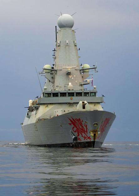 HMS Dragon, a gray warship with a red dragon painted on its bow, sails on the water.
