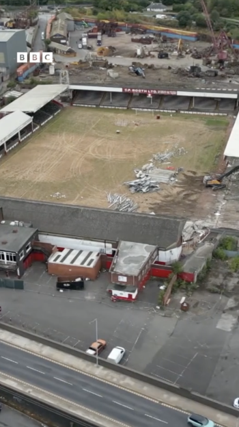 Aerial view of a stadium undergoing demolition, with rubble on the field and construction equipment nearby.