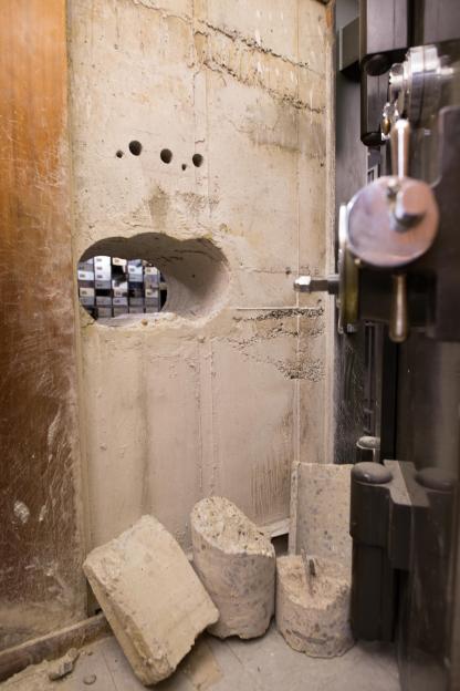 An image collage containing 2 images, Image 1 shows Inside the vault of the Hatton Garden Safe Deposit company after the robbery, showing overturned boxes and debris, Image 2 shows Holes drilled in a concrete vault wall, with broken concrete pieces on the floor