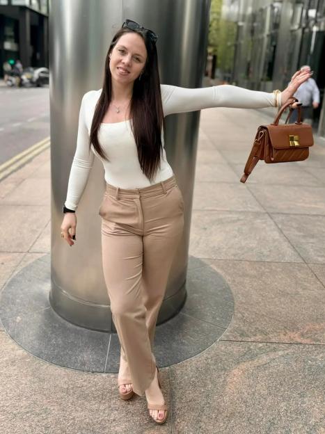 Woman in white shirt and tan pants holding a brown handbag.