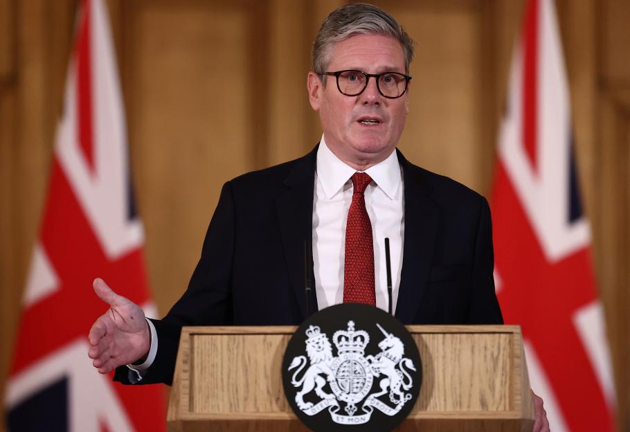 Sir Keir Starmer speaking at a press conference, with the Union Jack flag visible in the background.
