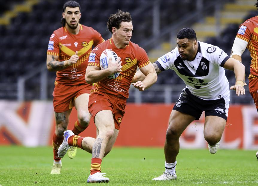 A rugby player in a red jersey runs with the ball while another player in a black and white jersey attempts to tackle him.