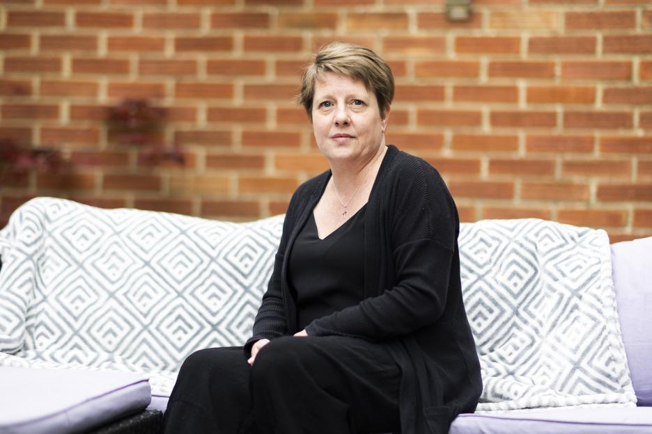Natalee Gibbings sits on a couch in front of a brick wall.