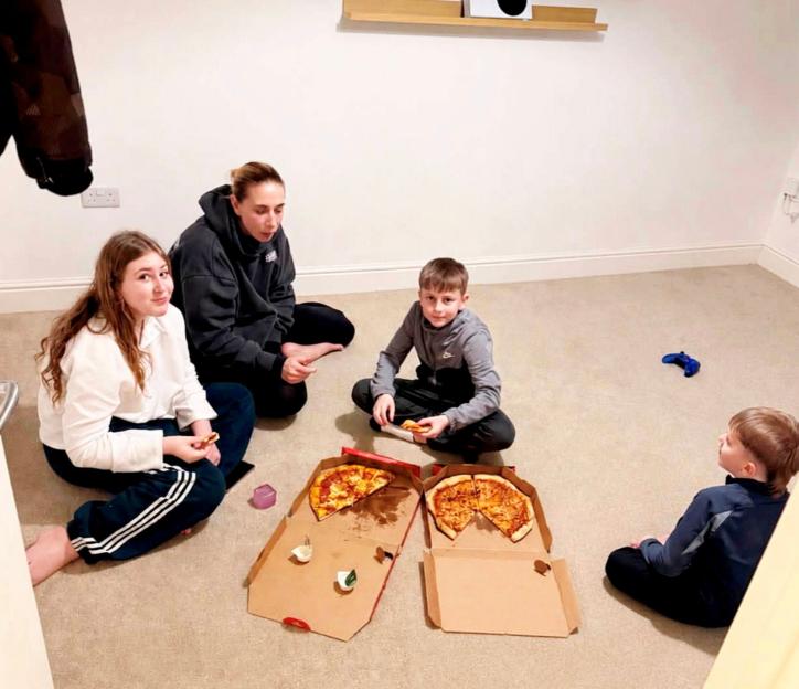 Three children and one adult eating pizza on the floor, watching TV.
