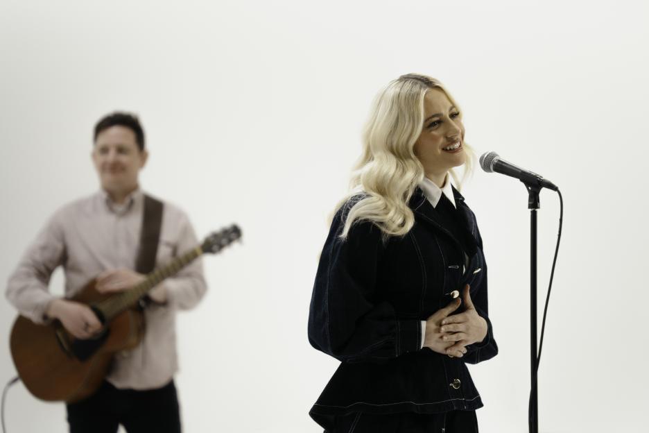 Pixie Lott singing into a microphone with a guitarist in the background.