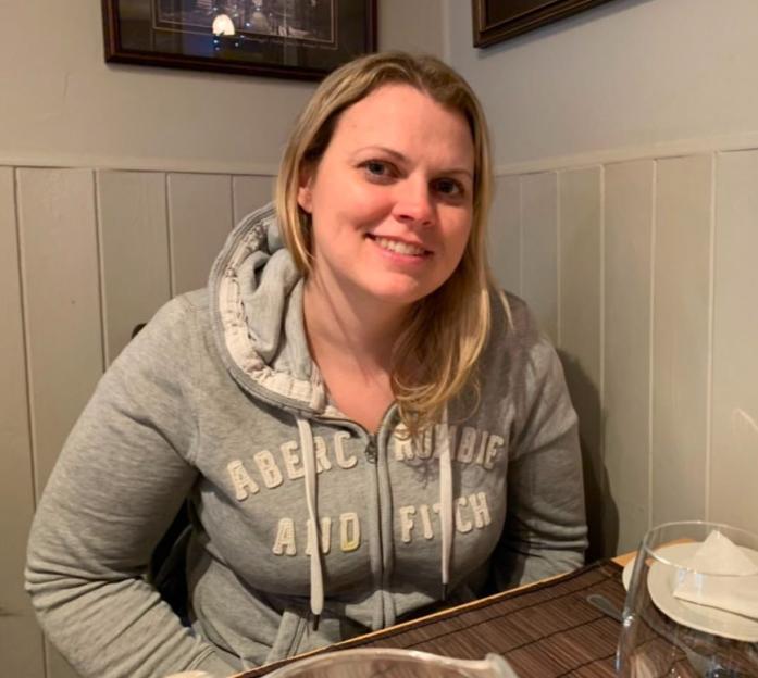Lois Kinder, 44, smiling while sitting at a table with glasses and plates.