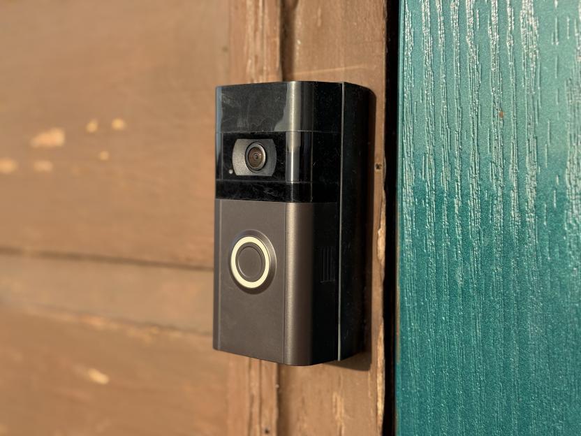 Smart doorbell camera mounted on a brown door frame next to a teal door.