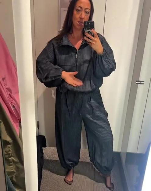 A woman trying on a striped dark blue tracksuit in a fitting room.