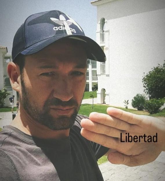 A man wearing an Adidas hat, with the word "Libertad" written on his outstretched hand.