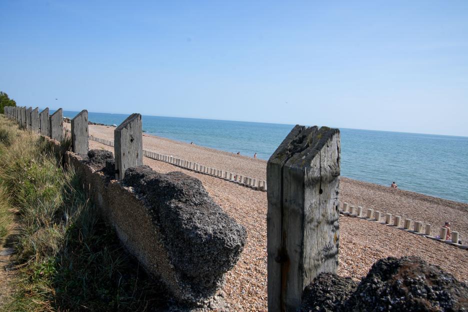 A nudist beach viewed from behind a weathered wooden fence.