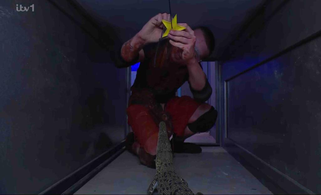 Aitch holding a star while a crocodile lurks nearby during a Bush Tucker Trial.