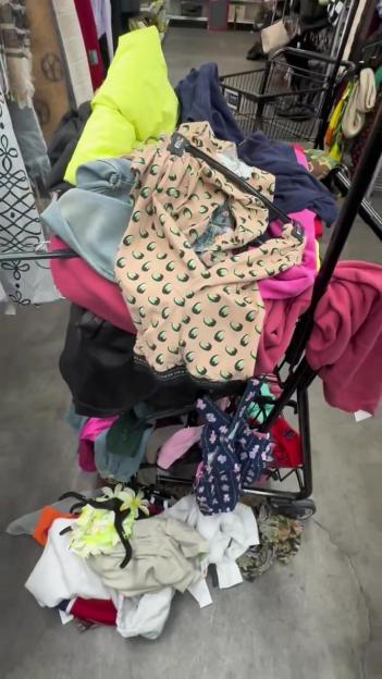 A shopping cart overflowing with clothes, including a beige top with green crescent moons.