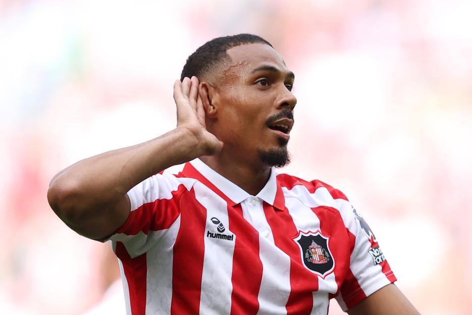 Sunderland player in a red and white striped jersey holds his hand to his ear.