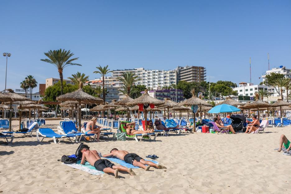 A sunny beach scene with people relaxing on lounge chairs and under straw umbrellas.