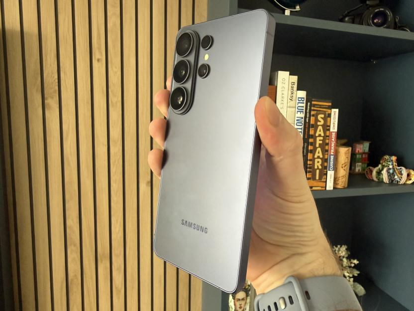 A hand holding up a gray Samsung smartphone, showing its back with multiple cameras.