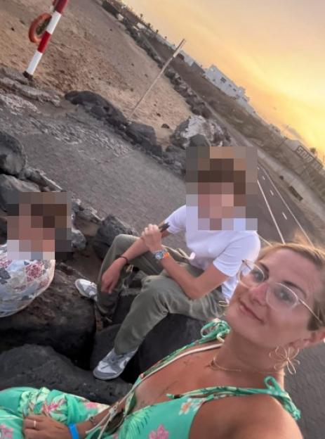 A woman taking a selfie with two men sitting behind her on rocks, with a sunset sky in the background.