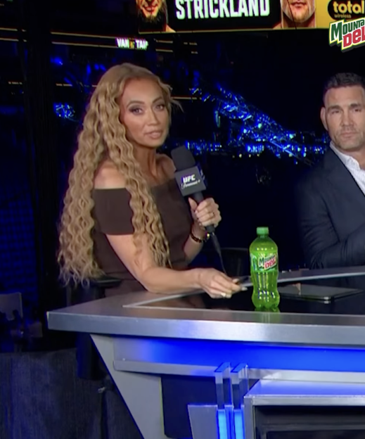 A woman holding a microphone and a man sitting at a desk with a bottle of Mountain Dew.