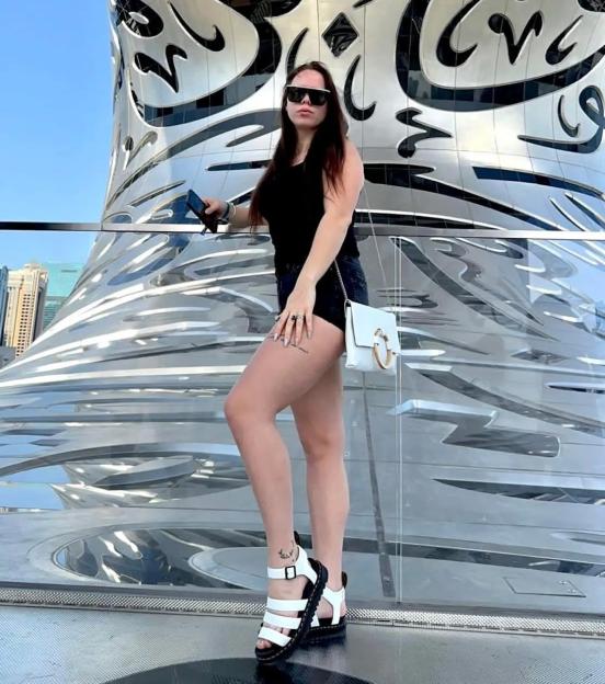 A woman in sunglasses and black shorts poses in front of the Museum of the Future in Dubai.