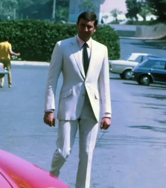 George Lazenby as James Bond in a white suit, walking on a street with cars in the background.