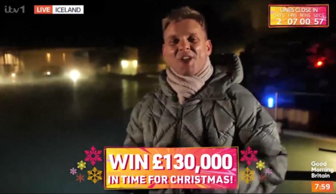 A man bundled in winter clothing stands outdoors at night in Iceland, with a "Win £130,000" graphic overlaid on the screen.