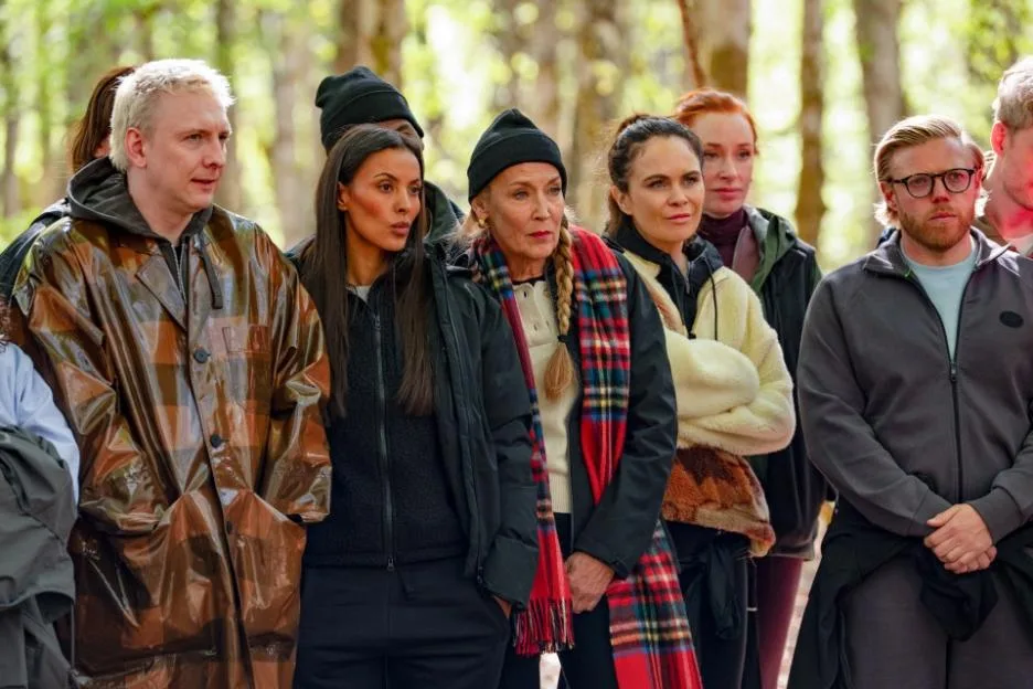 The cast of The Celebrity Traitors gathered outdoors in a wooded setting.