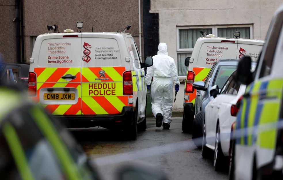 A forensic investigator in a white hazmat suit walks between two police vans at a crime scene.