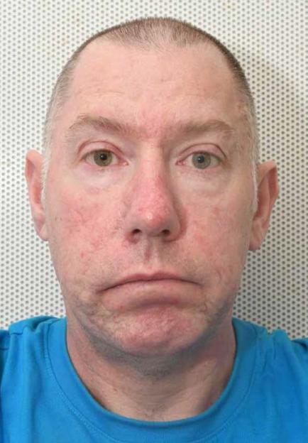 A mugshot of a man named Greer, with a receding hairline and green eyes, wearing a blue shirt.