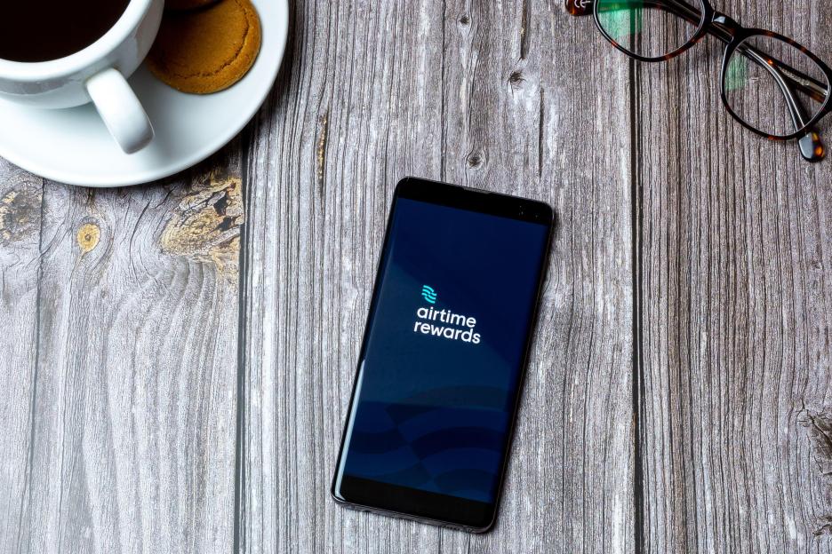 A mobile phone displaying the Airtime Rewards app on a wooden table.