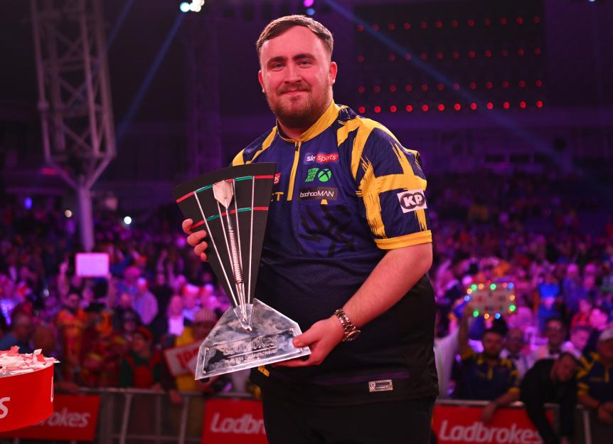 Luke Littler smiling and holding the Ladbrokes Players Championship trophy.