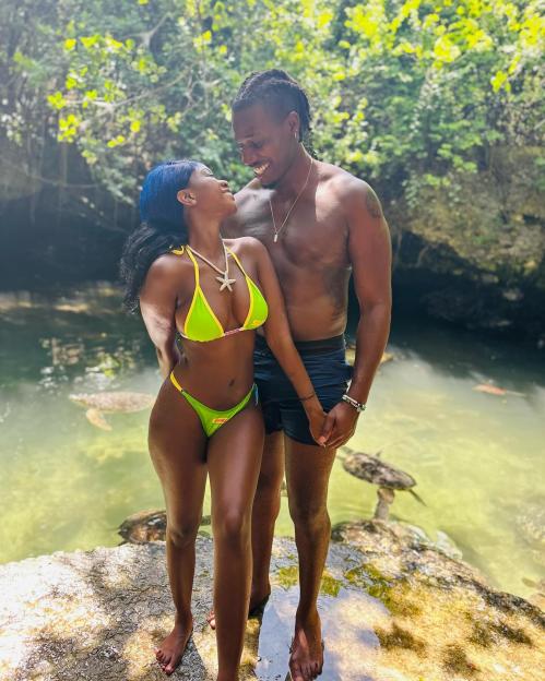 Tanya and Shaq posing on a rock in a clear body of water with turtles swimming, framed by lush greenery.
