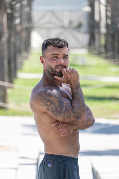 Tommo Holbrook, a shirtless, tattooed man, poses while looking to the right.